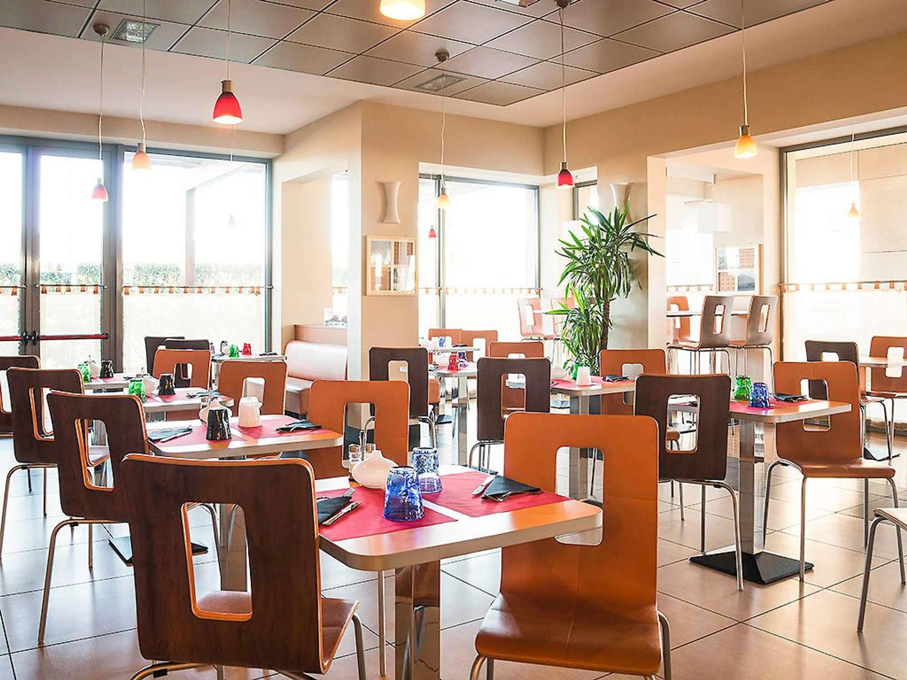 A restaurant with multiple tables and chairs, large windows, and hanging pendant lights.