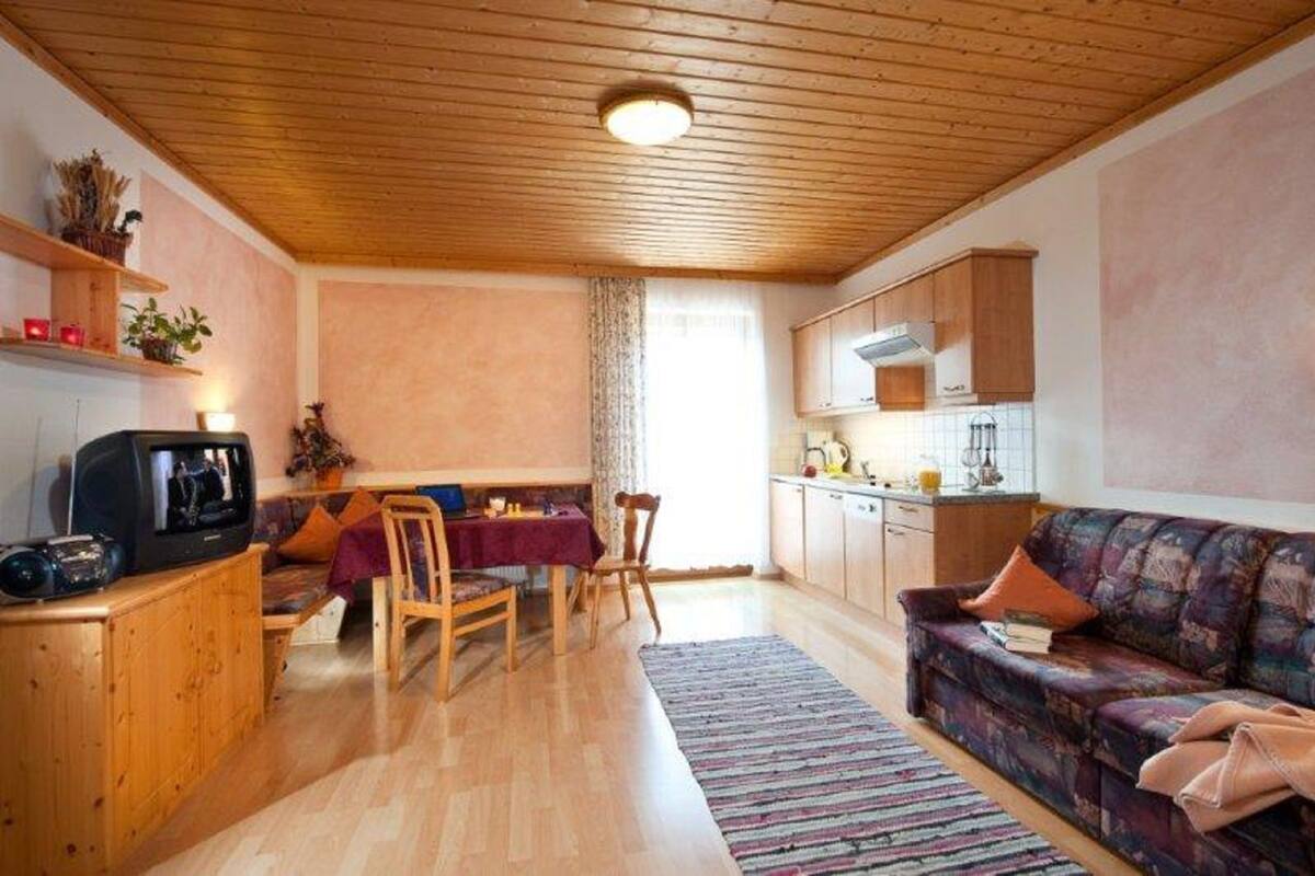 Ein gemütliches Wohnzimmer mit Holzboden, ein Essbereich mit Tisch und Stühlen sowie eine Küche mit Holzausstattung.