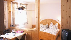 Una habitación de madera con una cama, una mesa con sillas, un televisor y un ventanal con cortinas.