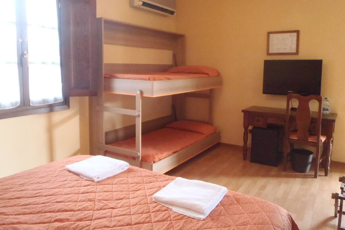 Une chambre avec des lits superposés, une télévision, un bureau et une fenêtre.
