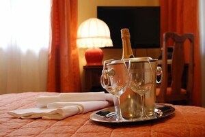 Una habitación con una cama, una mesita de noche con lámpara, una botella de champán y dos copas de vino sobre una bandeja.