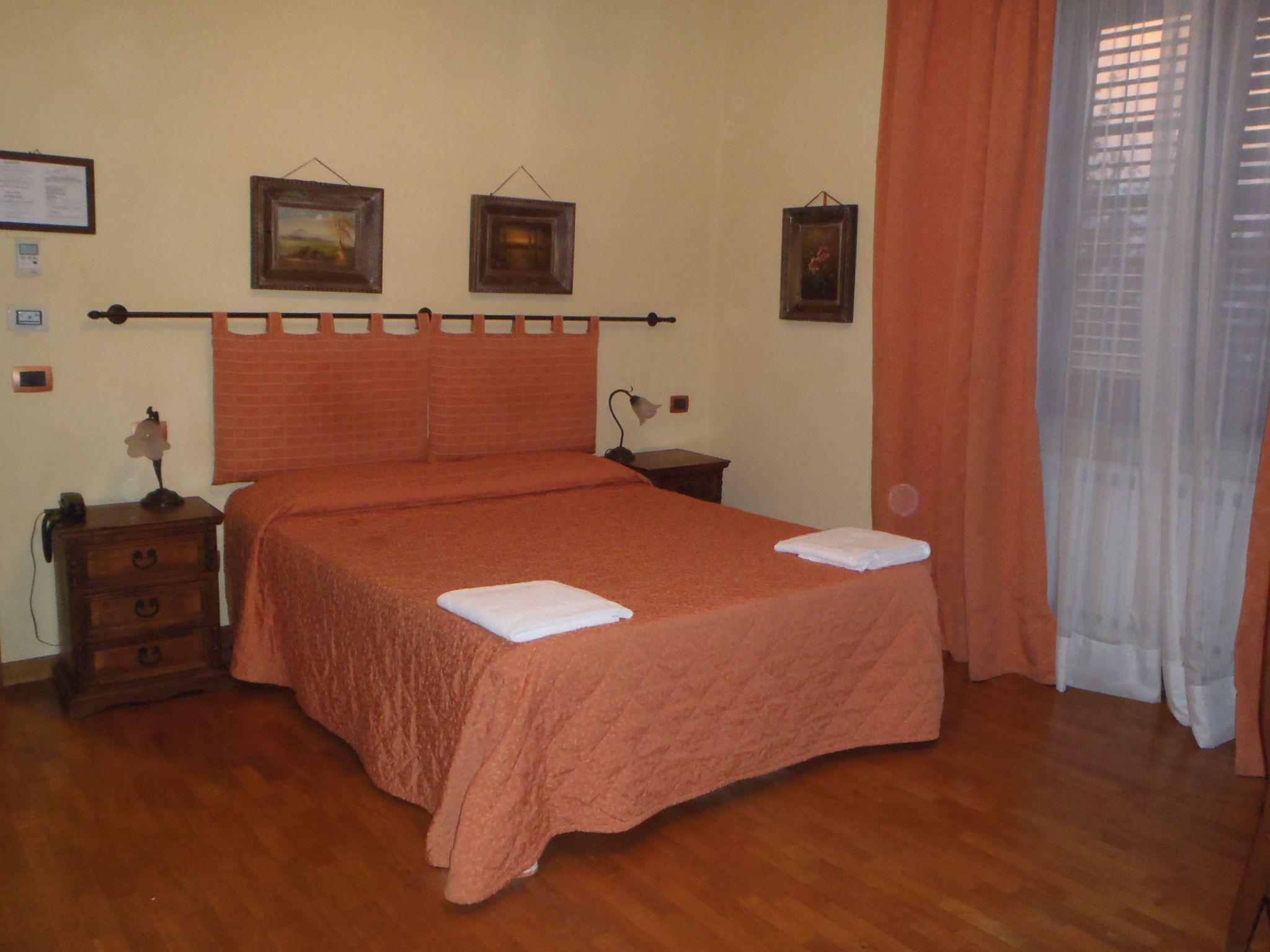 Une chambre à coucher avec un lit, une table de chevet, une commode et une fenêtre avec des rideaux.