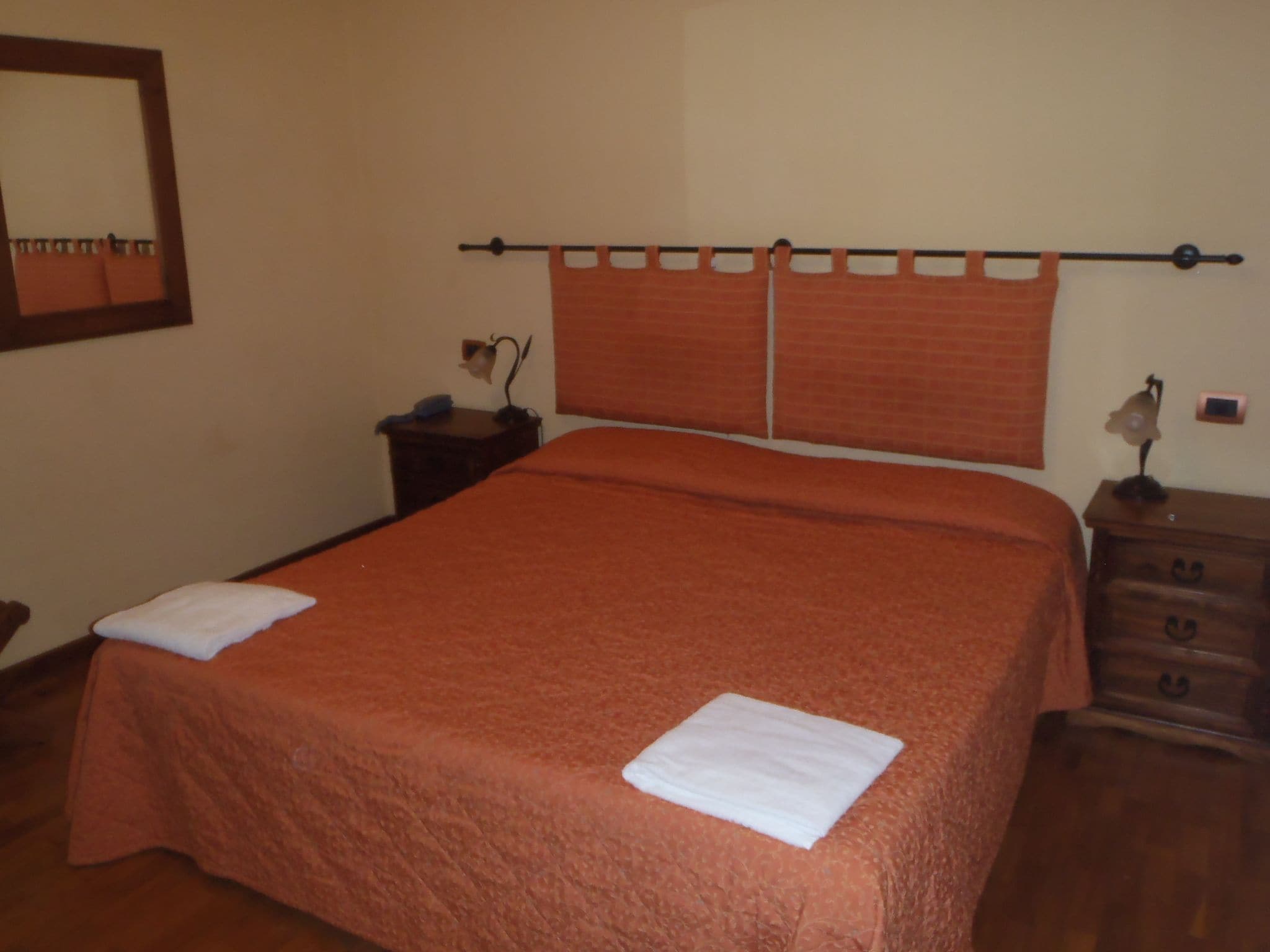 Una cama bien tendida con cabecera, una mesita de noche con lámpara y un pequeño aparador.