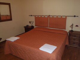 Una cama bien tendida con cabecera, una mesita de noche con lámpara y un pequeño aparador.