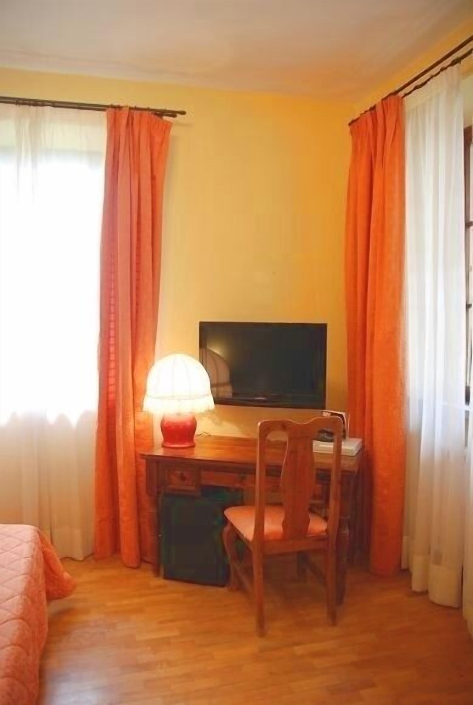 A room with a wooden desk, a chair, a television, and a lamp.