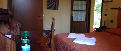 A room with a bed, a wooden desk, a chair, a bottle of water, and a door leading outside.