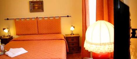 A hotel room with a bed, a nightstand, a lamp, and a television.