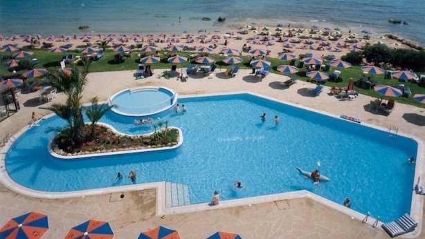 Una gran piscina con varias pistas, rodeada de sombrillas y sillas de descanso, con vista al océano.