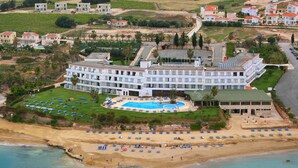 Vista aérea de un resort con una piscina grande, múltiples sombrillas en la playa y acceso directo a la orilla.