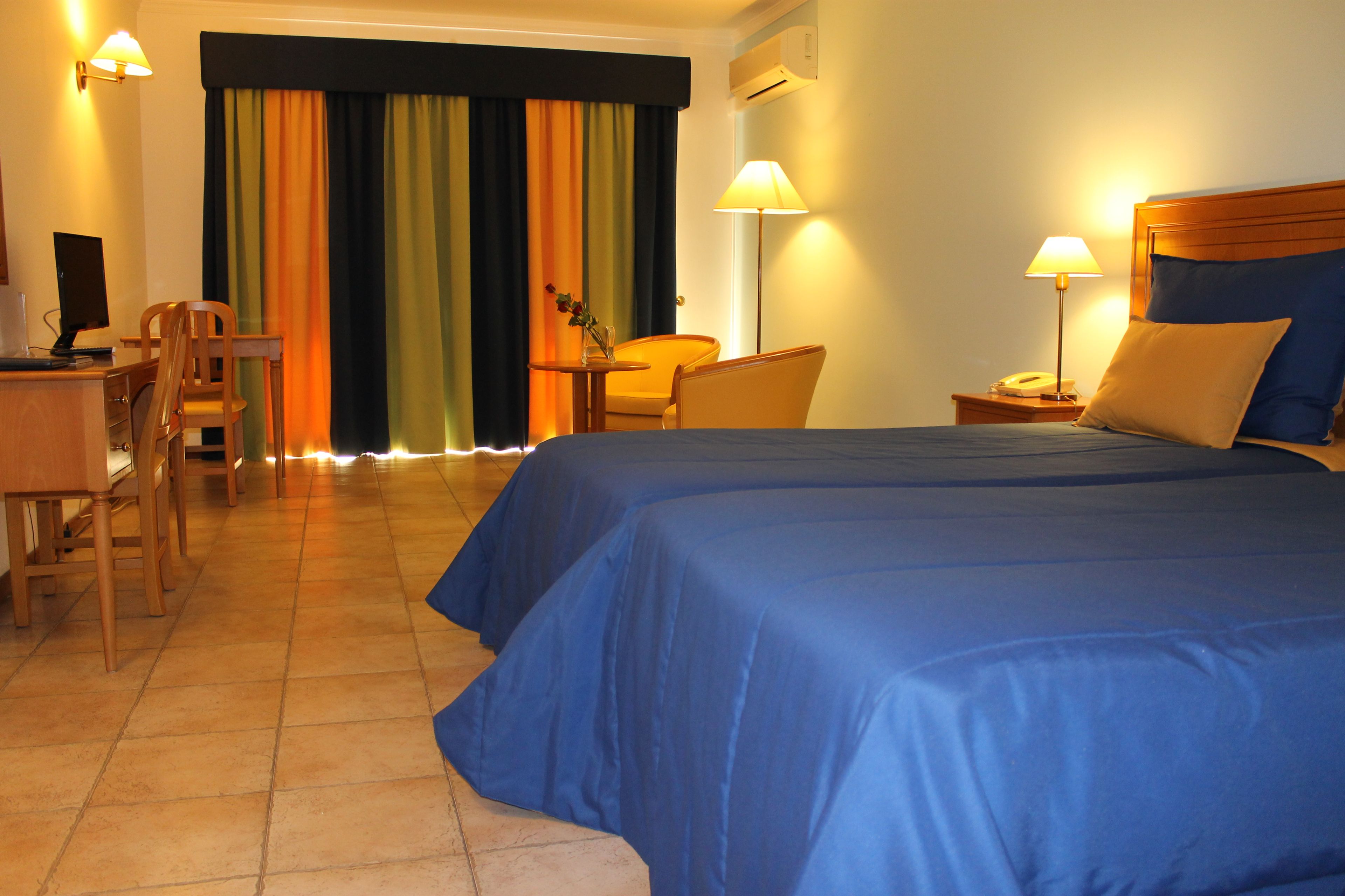 A hotel room with a large bed, two chairs, a desk, a lamp, and a telephone on a bedside table.
