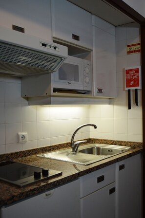 A kitchen with a granite countertop, stainless steel sink, white cabinets, and a microwave. - Cais da Oliveira (Santa Cruz)