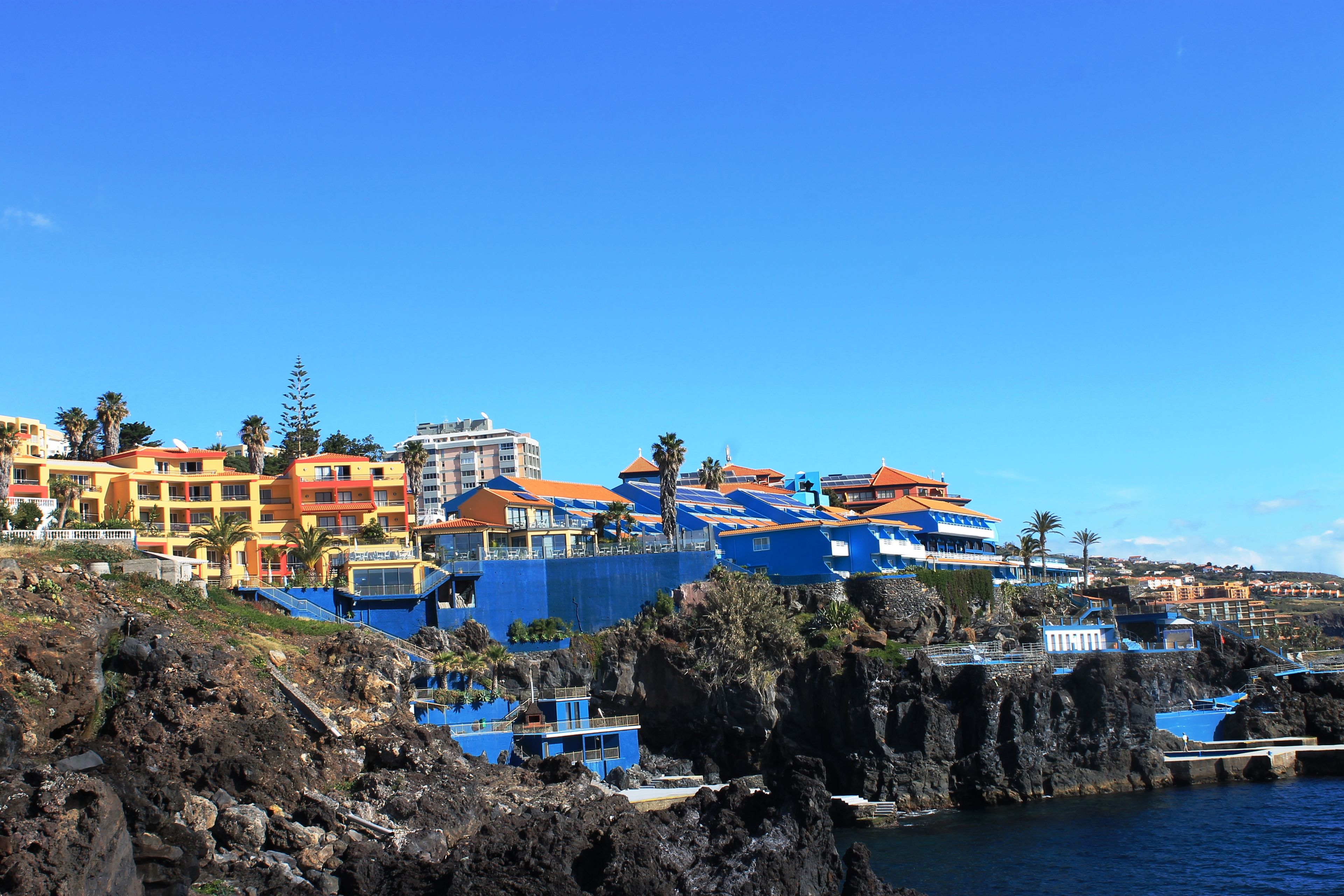 A coastal town with colorful buildings, rocky terrain, and a clear blue sky.