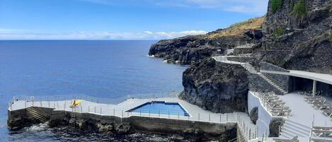 Un área de piscina con vista al océano, rodeada de acantilados rocosos y una escalera de piedra.