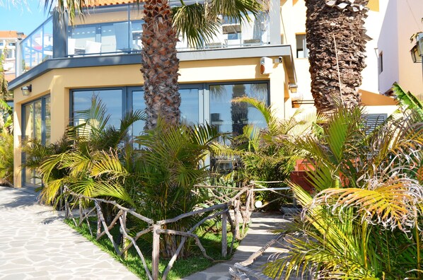 A modern building with large windows, a stone pathway, and tropical plants. - Cais da Oliveira (Santa Cruz)