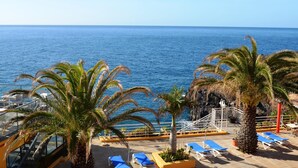 A deck with blue lounge chairs and palm trees overlooking the sea. - Cais da Oliveira (Santa Cruz)