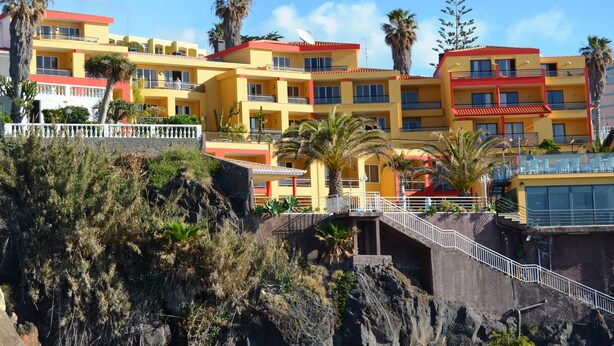 A multi-story hotel with balconies, located on a hillside with palm trees and rocky terrain. - Cais da Oliveira (Santa Cruz)