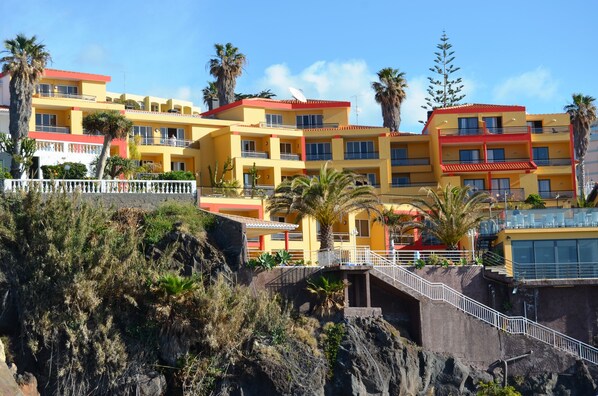 A multi-story hotel with balconies, located on a hillside with palm trees and rocky terrain. - Cais da Oliveira (Santa Cruz)