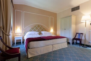 Una habitación de hotel con una cama, dos mesitas de noche, una silla, un armario y una lámpara.