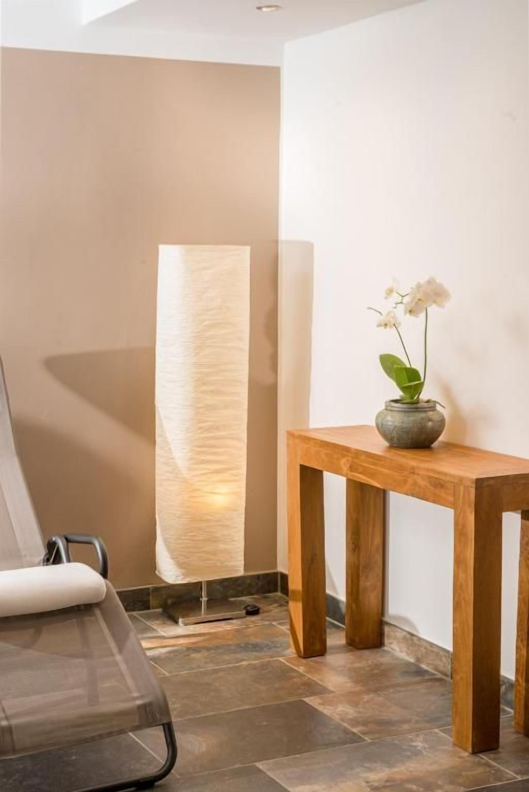 A room with a wooden table, a potted plant, and a large textured wall.
