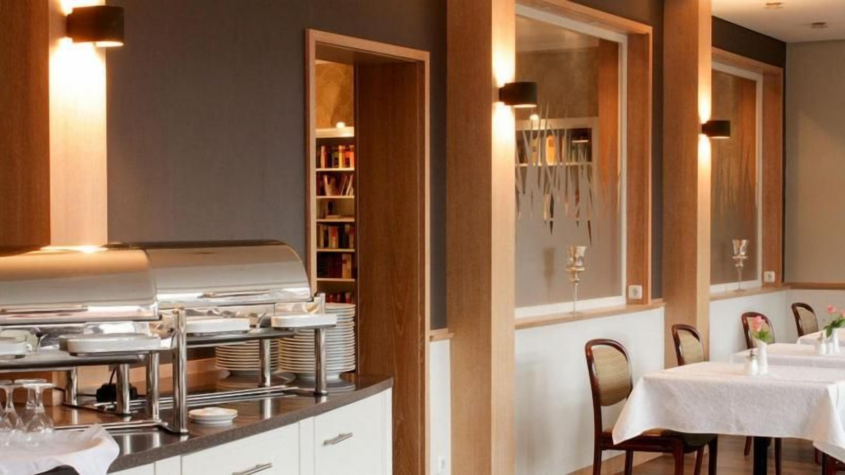 Un buffet disposé sur une table en acier inoxydable, un espace repas avec des tables et des chaises, et un lustre décoratif.
