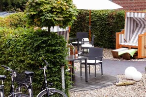 An outdoor seating area with wicker furniture, a bicycle, and a hedge. - AKZENT Hotel Dorn (Büsum)