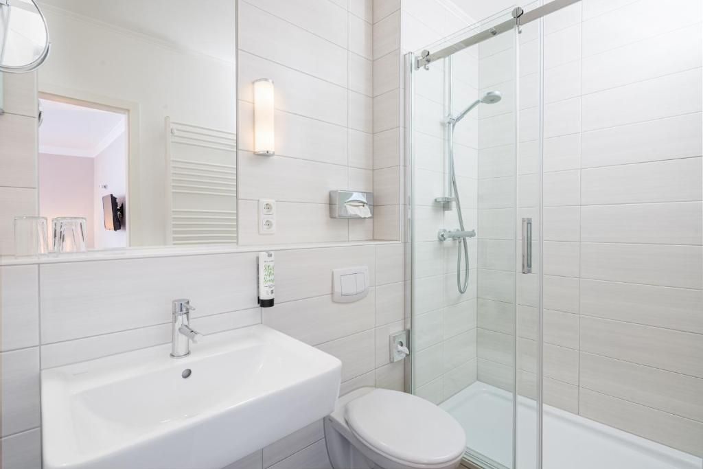 Un baño moderno con lavamanos blanco, inodoro y ducha con mampara de vidrio.
