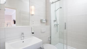 Un baño moderno con lavamanos blanco, inodoro y ducha con mampara de vidrio.