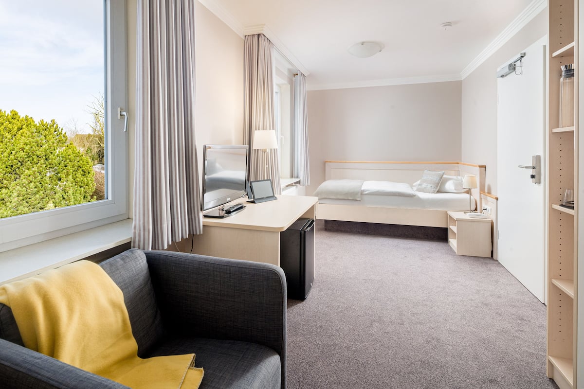 Una habitación de hotel moderna con cama, escritorio y vistas a zonas verdes.