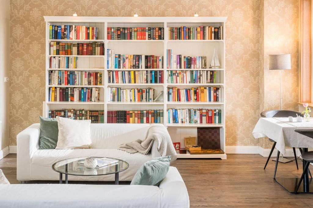 Ein Wohnzimmer mit einem weißen Sofa, einem Glastisch, einem Bücherregal voller Bücher und einem Essbereich mit Tisch und Stühlen.