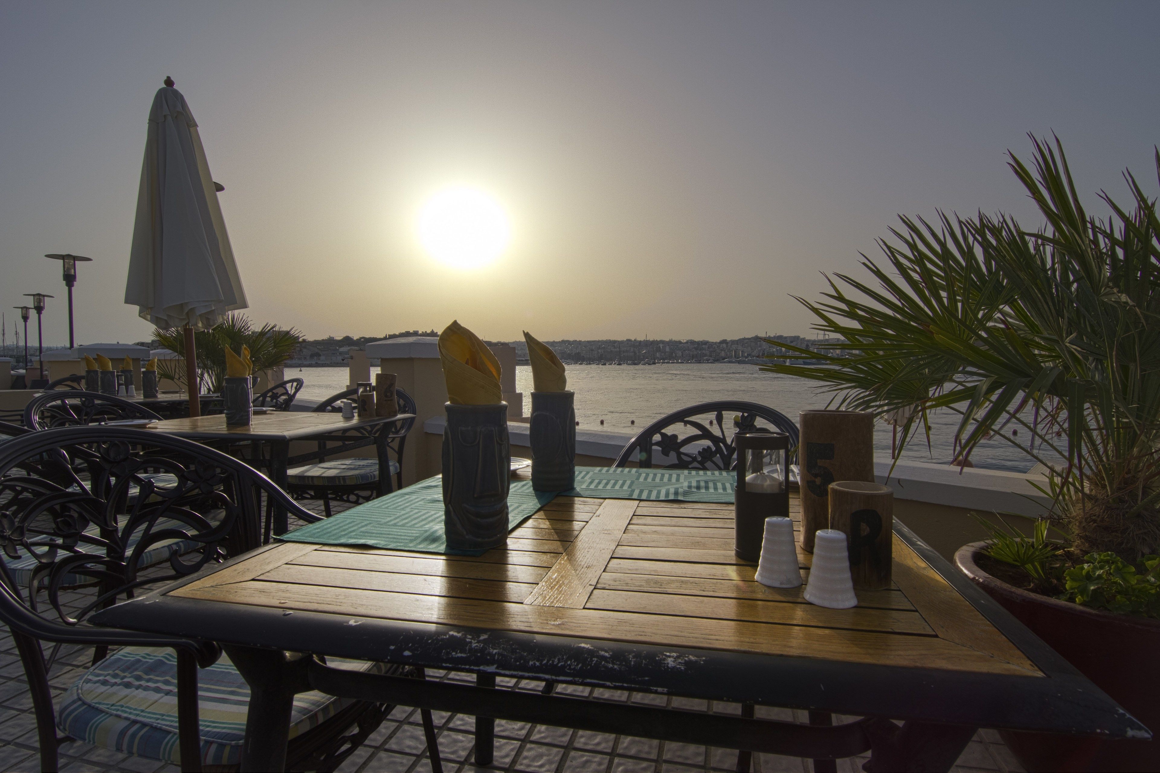 Een houten tafel met stoelen en uitzicht op de ondergaande zon boven het water.