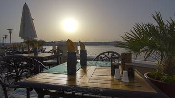 Een houten tafel met stoelen en uitzicht op de ondergaande zon boven het water.