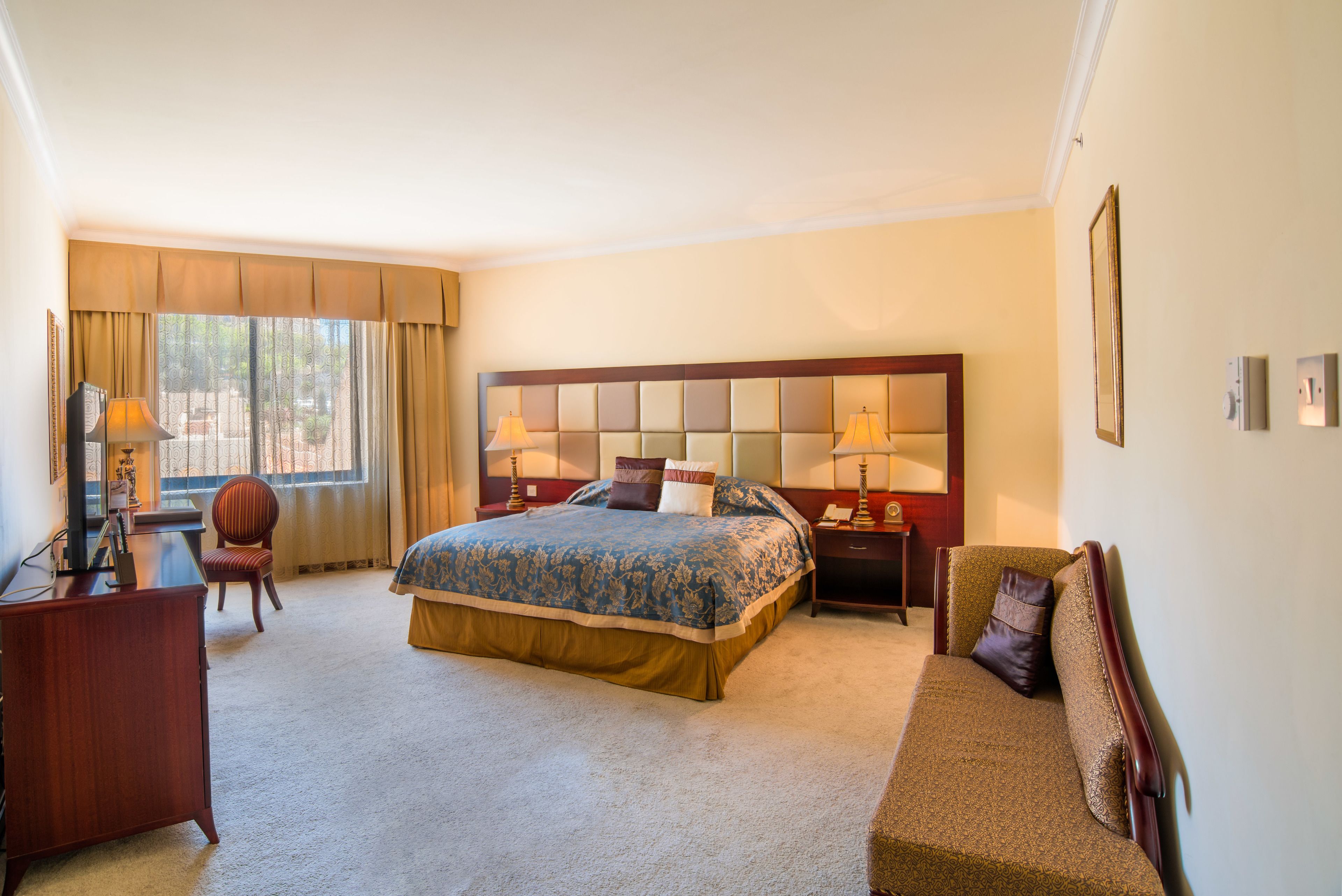 A hotel room with a large bed, a desk, a chair, and a sofa.