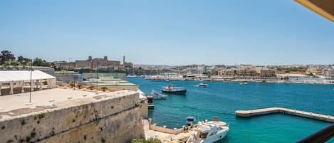 A coastal cityscape with a marina, a large building with a flat roof, and a stone wall.