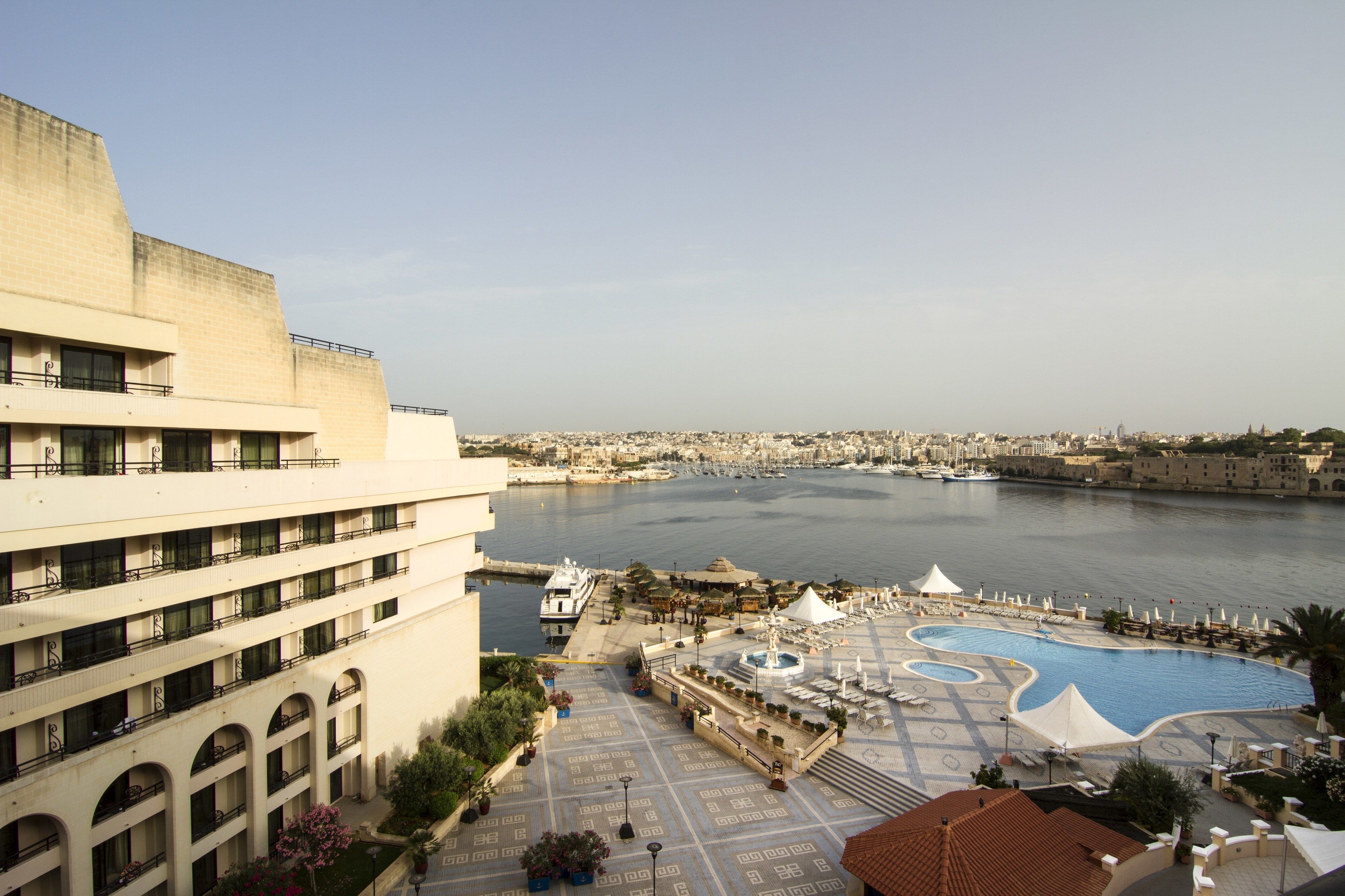 A hotel with a pool area, a view of the sea, and a cityscape in the background.