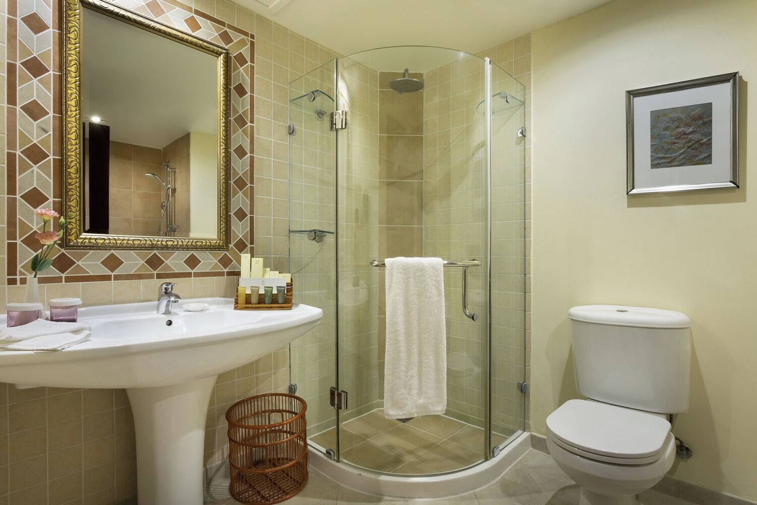 Un baño con ducha de vidrio, lavamanos blanco con artículos de aseo y retrete.