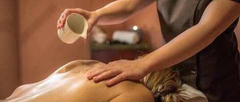 A person receiving a back massage in a room with a warm ambiance, featuring a name tag on the masseuse's shirt.
