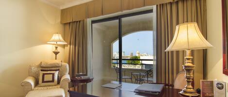 A hotel room with a large window, a desk, a chair, and a lamp.