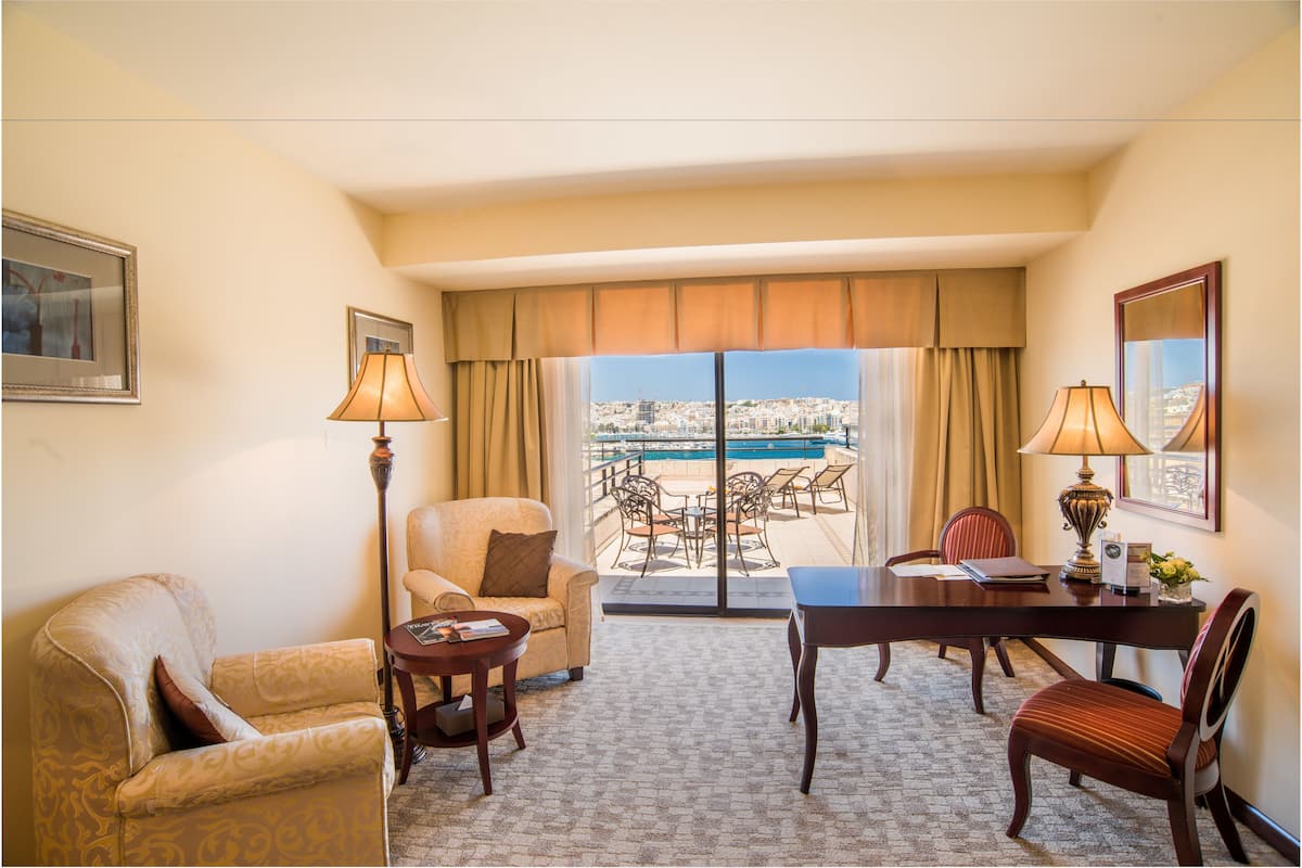 A hotel room with a balcony, a dining table, two chairs, a sofa, and two lamps.