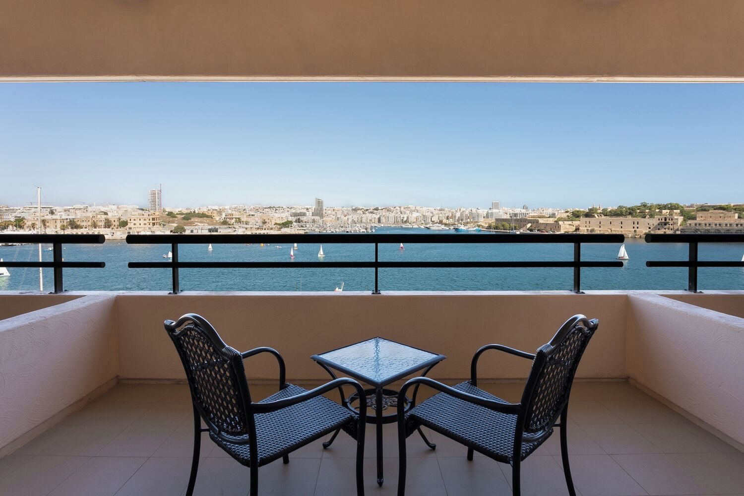 Un balcón con dos sillas y una mesa, con vista a la ciudad y al mar.