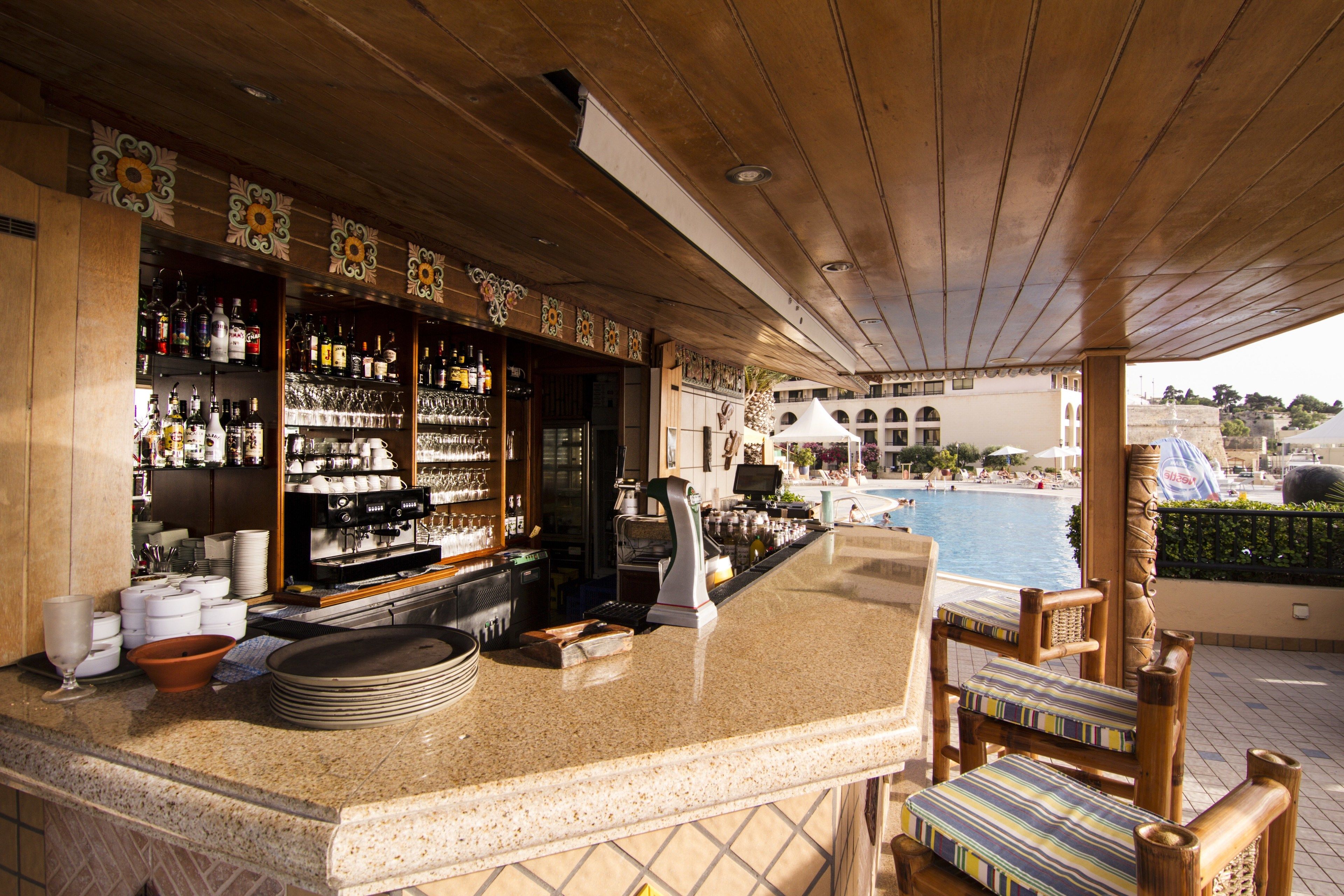 Zona de bar con vista a la piscina, techo de madera y estanterías llenas de botellas.