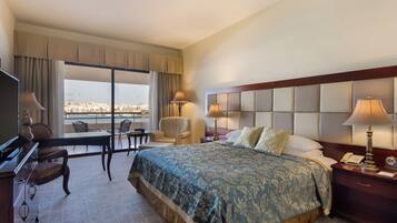 Habitación de hotel con una cama grande, un escritorio, una silla y vistas a la ciudad desde la ventana.