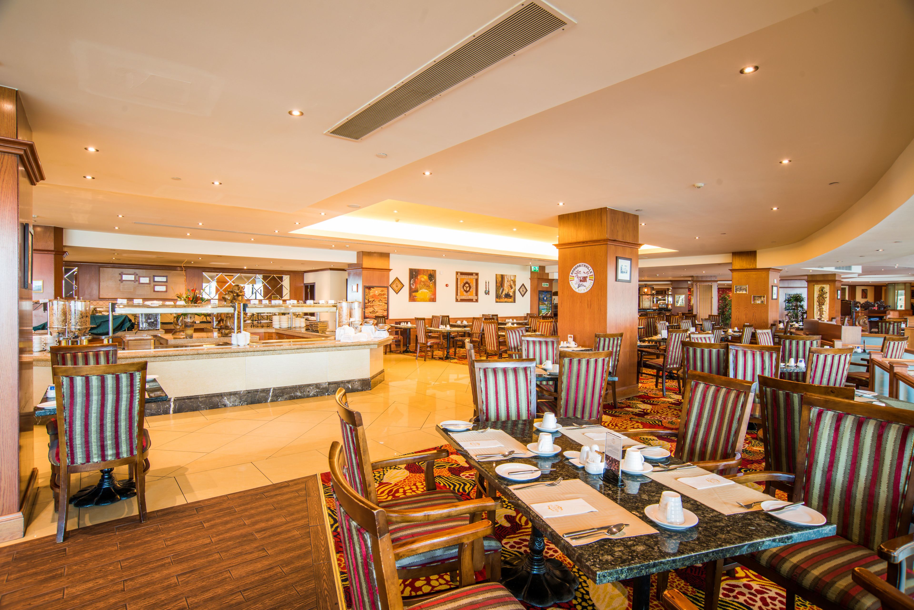 Un vaste espace de restauration dans l’hôtel, avec de nombreuses tables et chaises, un bar central et un buffet.
