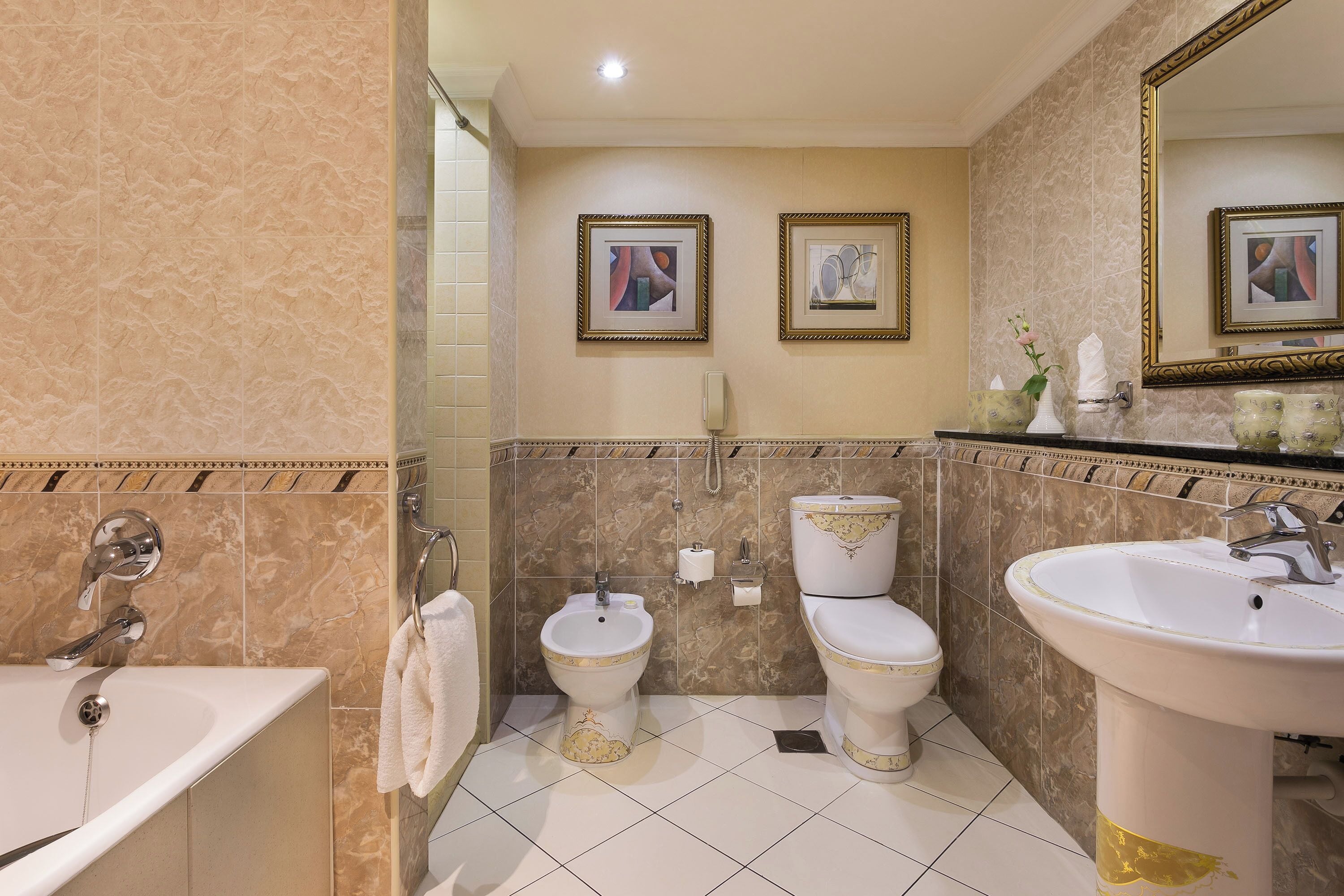 A bathroom with a bathtub, a bidet, a toilet, and a sink. There are framed pictures on the wall and a mirror above the sink.