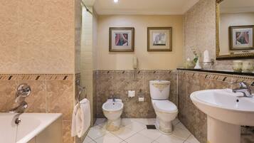 A bathroom with a bathtub, a bidet, a toilet, and a sink. There are framed pictures on the wall and a mirror above the sink.