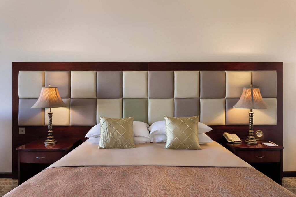 Une chambre d’hôtel avec un grand lit, deux tables de chevet, des lampes et une tête de lit dotée de panneaux rembourrés.