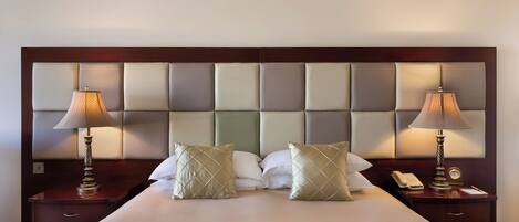 Habitación de hotel con una cama grande, dos mesitas de noche, lámparas y un cabecero con paneles acolchados.