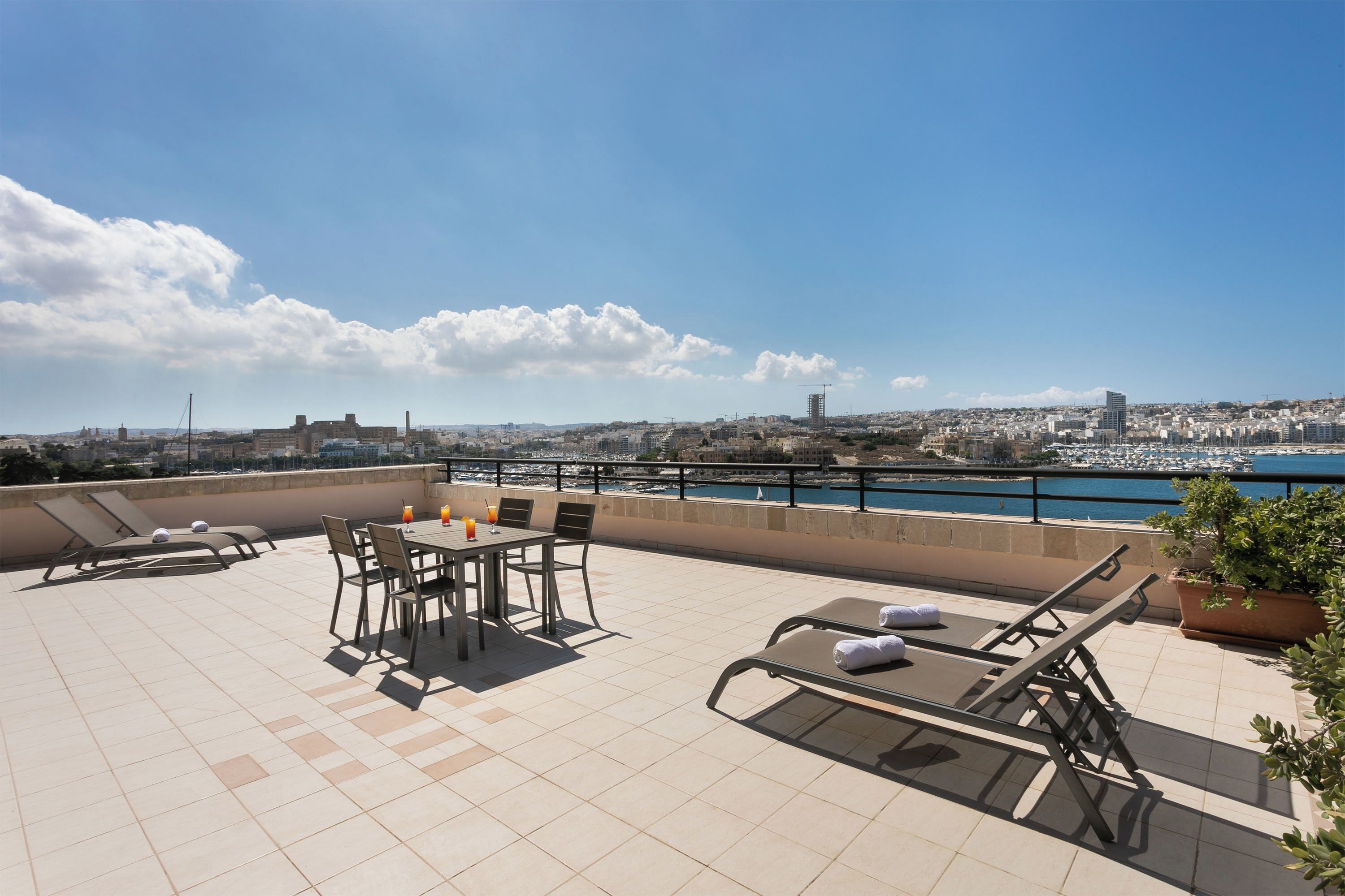 A rooftop terrace with a table and chairs, lounge chairs, and a view of the city and water.