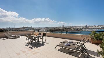 A rooftop terrace with a table and chairs, lounge chairs, and a view of the city and water.