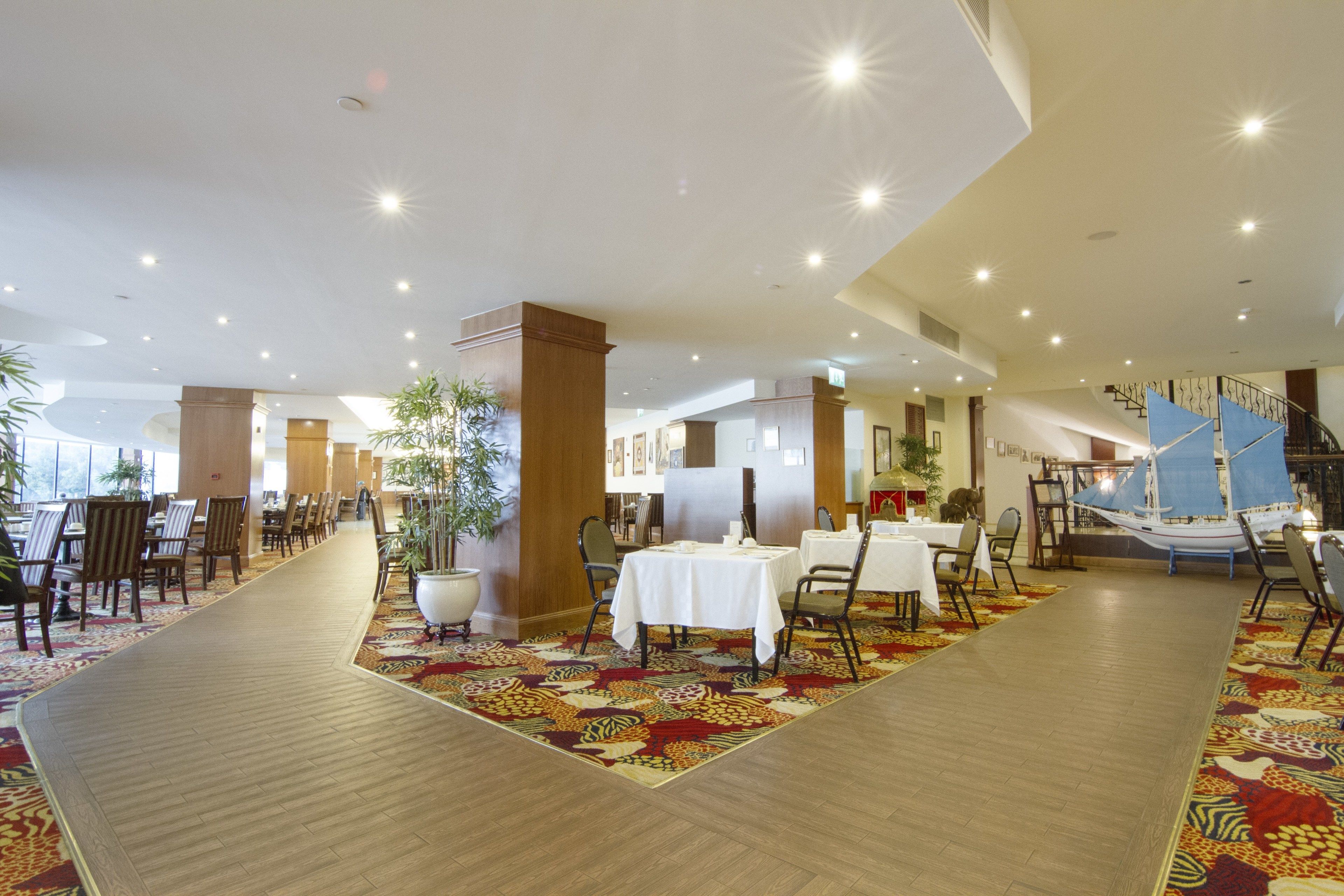A spacious hotel lobby with multiple dining areas, a central column, and a decorative sailboat.