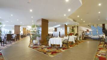 A spacious hotel lobby with multiple dining areas, a central column, and a decorative sailboat.